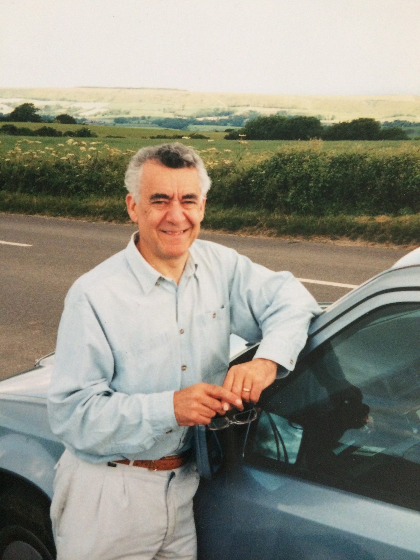 Brian smiling, leaning on his car in the countryside