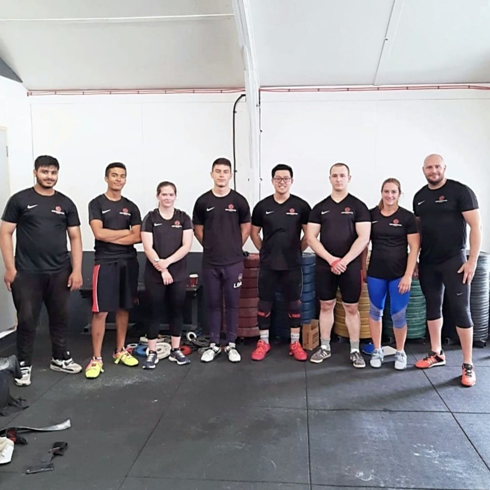 Eight Woking lifters in black club shirts standing in a row in the gym