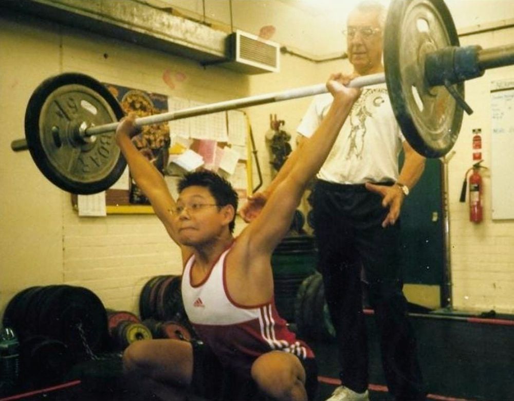 Brian standing behind Chris Chea as he holds a barbell overhead at the bottom of a snatch